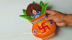 a hand holding an orange decorated pot with leaves and jewels on it's side