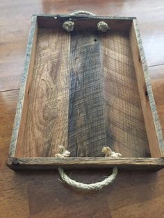 a wooden box with rope on the bottom and two hooks in the middle sitting on top of a wood floor