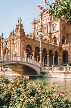 a bridge over a river in front of a large building with arches and flowers on it