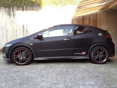 a black sports car parked in front of a building with red rims on it