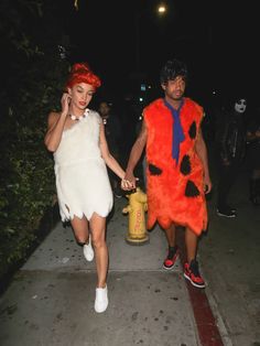 two people in costumes walking down the street at night with fire hydrant behind them