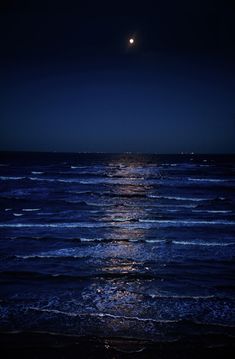 the moon is shining brightly over the ocean at night with waves coming in to shore