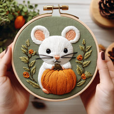 a person holding a hoop with a small embroidered mouse on it's face and an orange pumpkin in the other hand