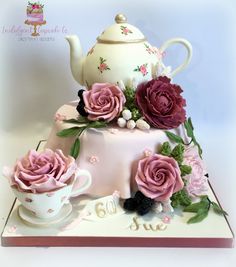 a cake decorated with pink roses and teapots on top of a white table