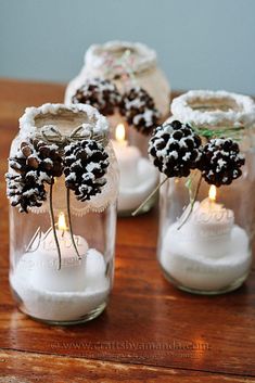 three mason jars filled with candles and snow covered pineconis are sitting on a table