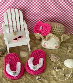 two crocheted slippers are sitting on the sand next to a doll's chair and seashells