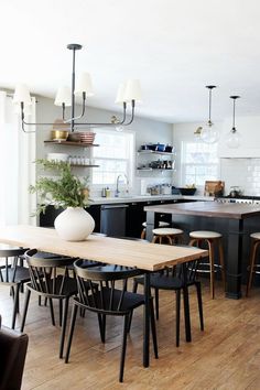 a dining room table and chairs in a kitchen with wood flooring, white walls and black cabinets