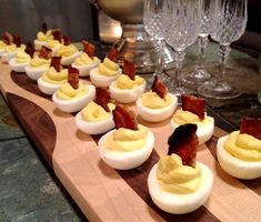 deviled eggs with bacon are lined up on a wooden board next to wine glasses