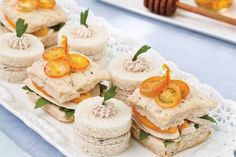 small sandwiches are arranged on a white platter with orange slices and green leafy garnishes