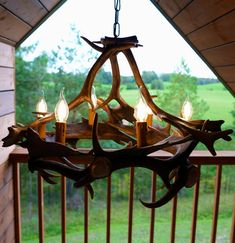 a chandelier made out of antlers on a porch with grass and trees in the background