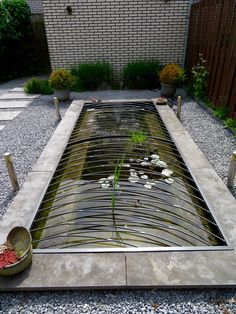 a small pond in the middle of a graveled area with plants and rocks around it