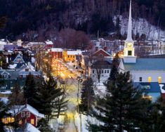 a small town is lit up at night in the mountainside with snow on the ground