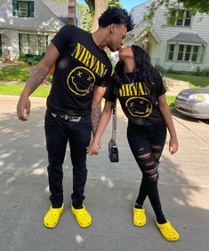 a man and woman standing next to each other in front of a house with yellow shoes