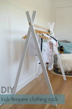 a rack with clothes hanging on it next to a white wall and wood flooring