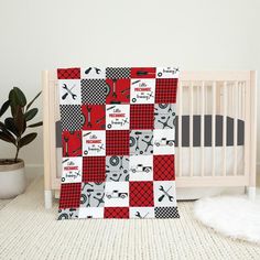 a baby crib with a red and black patchwork quilt next to a potted plant