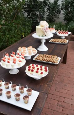 several desserts are arranged on white plates on a wooden table with greenery in the background