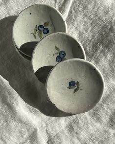 three white bowls with blue flowers on them sitting on a tableclothed surface in the sunlight