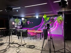 the room is set up for an event with purple lighting and black tables, chairs, and plants