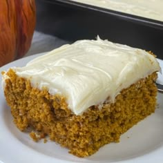 a piece of carrot cake with white frosting on a plate next to an apple