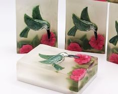 three glass boxes with hummingbirds on them and pink flowers in the bottom one is white