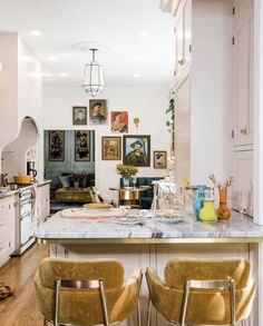 two yellow chairs sit at the center of this kitchen island with marble countertops and gold stools