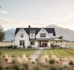 a large white house sitting in the middle of a lush green field with mountains in the background