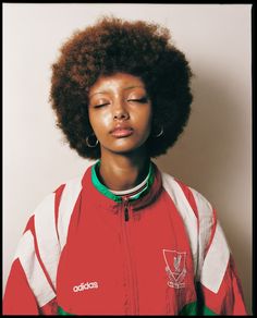 a woman with an afro standing in front of a white wall wearing a red and green jacket