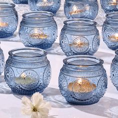 many blue glass jars are lined up on a table next to a white flower and some candles