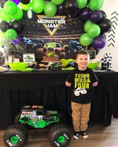 a young boy standing in front of a table with monster trucks and balloons on it