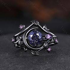 a fancy ring with purple stones and leaves on the sides, sitting on a black surface