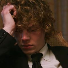 a young man in a suit and tie holding his head to his ear with one hand