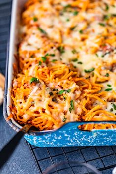 a blue casserole dish filled with pasta and meat covered in cheese, parsley