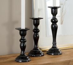 two black candlesticks sitting on top of a wooden table next to a mirror