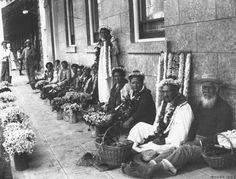 an old black and white photo of men sitting on the side of a building with flowers