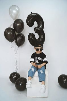 a young boy sitting on top of a white chair with balloons in the shape of numbers