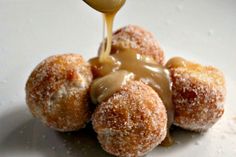 a spoon drizzling sauce onto some sugared doughnuts on a white plate