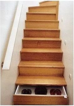 an open drawer under some stairs with shoes in the bottom compartment on one side and two pairs of black slippers on the other