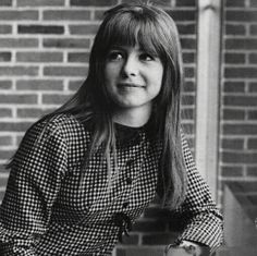 a black and white photo of a woman sitting in front of a brick wall with her hands on her hips