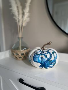 an octopus painted pumpkin sitting on top of a white dresser next to a vase and mirror