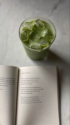 an open book sitting on top of a table next to a cup filled with ice cubes