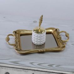 a white and gold tray with a feather on it, sitting on a table next to a mirror