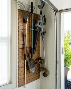 a wall mounted garden tool rack with gardening tools hanging on it's side, in front of a sliding glass door