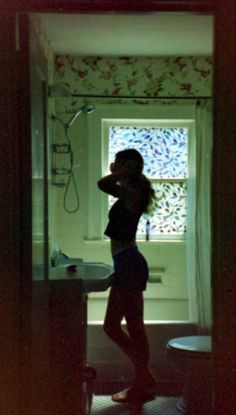 a woman standing in front of a bathroom sink next to a bathtub and window