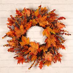 a wreath with autumn leaves and berries hanging on a brick wall in front of a white brick wall