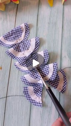 someone is cutting fabric with scissors on a wooden table next to flowers and other decorations