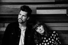 a man and woman sitting next to each other in front of a wooden wall,