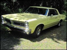 an old yellow car is parked in the grass