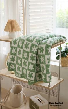 a green and white blanket sitting on top of a wooden shelf next to a lamp