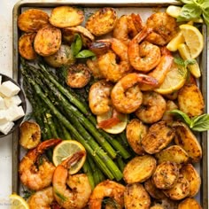 shrimp and asparagus on a baking sheet with lemon wedges