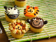 four cupcakes decorated to look like animals on a bamboo mat with decorations around them